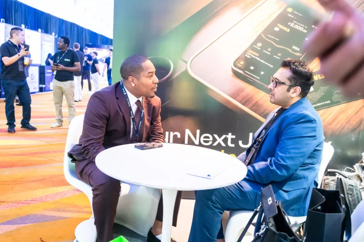 Two attendees in discussion at a table in the Travls booth